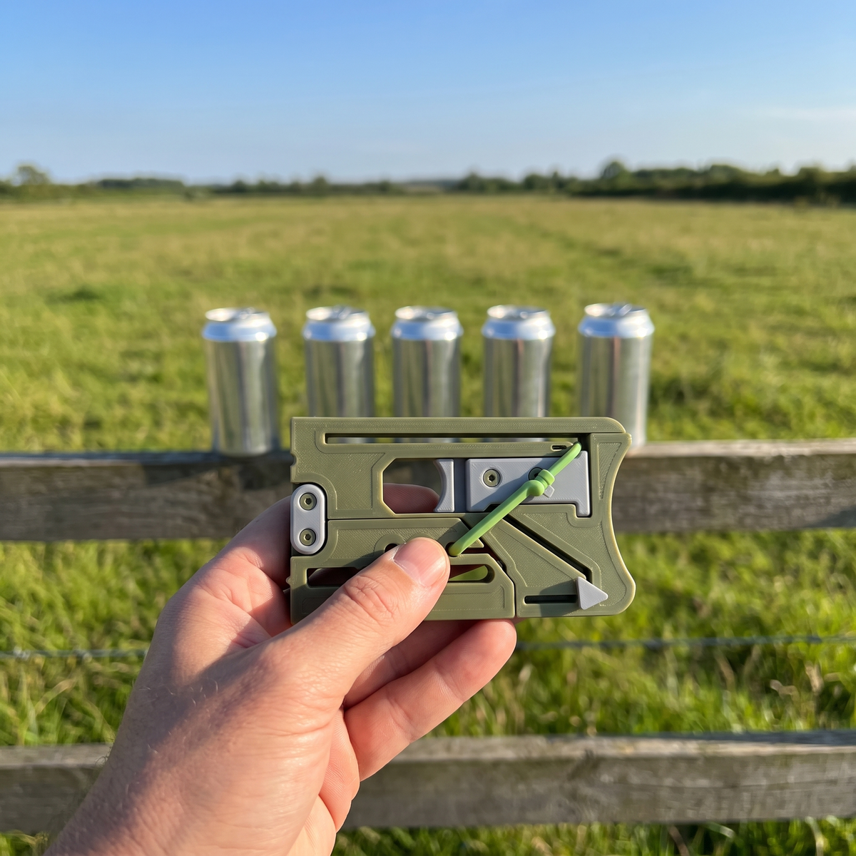 Green Sling Pop card slingshot held up in front of a row of cans